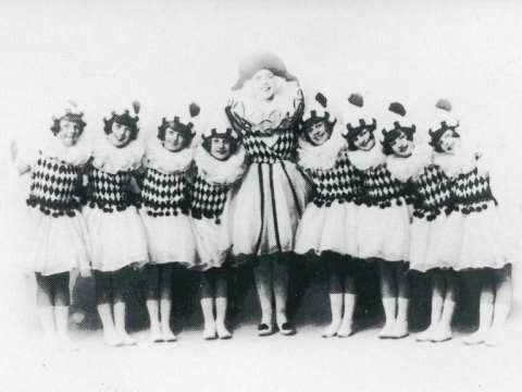 A black and white photograph of performer Gwladys Stanley with 8 young Sunbeam performers all wearing matching outfits.